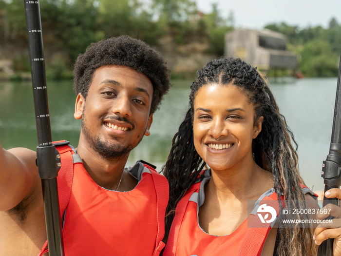 Portrait of smiling friends wearing life jackets and holding oar