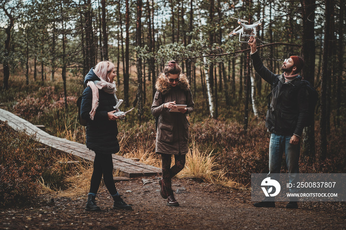 Bearded student is making photo using his drone, while his friends are watching something on the tablet.