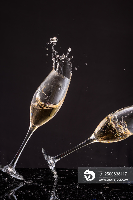 falling glasses with white wine champagne, splash and splatter on a black background