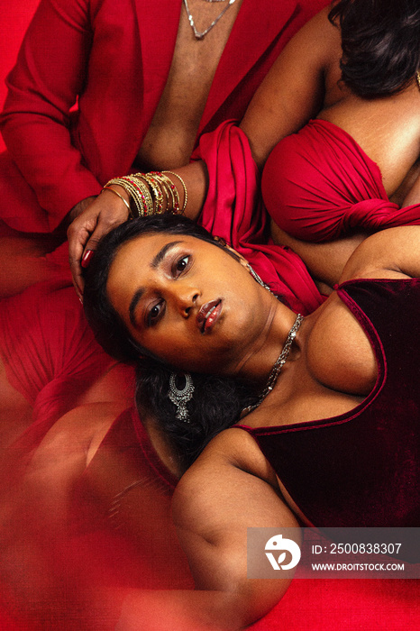 Group of Malaysian Indian individuals posing and laughing together against a red background, dressed in red clothing