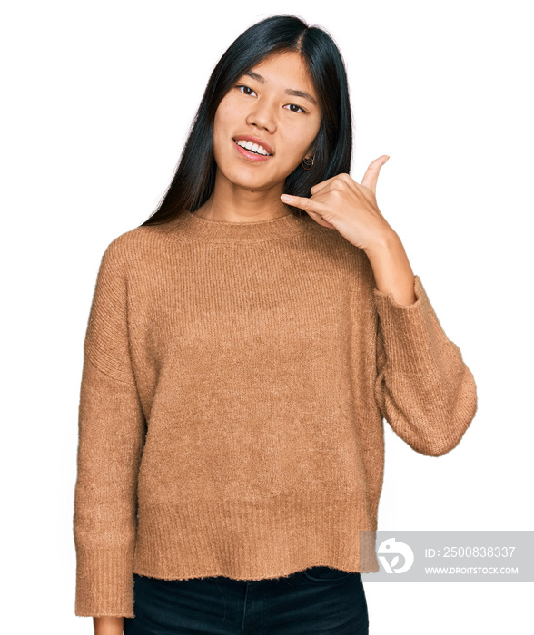 Beautiful young asian woman wearing casual winter sweater smiling doing phone gesture with hand and fingers like talking on the telephone. communicating concepts.