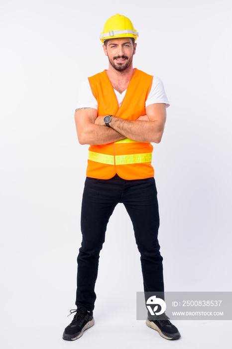 Full body shot of happy young bearded man construction worker smiling with arms crossed