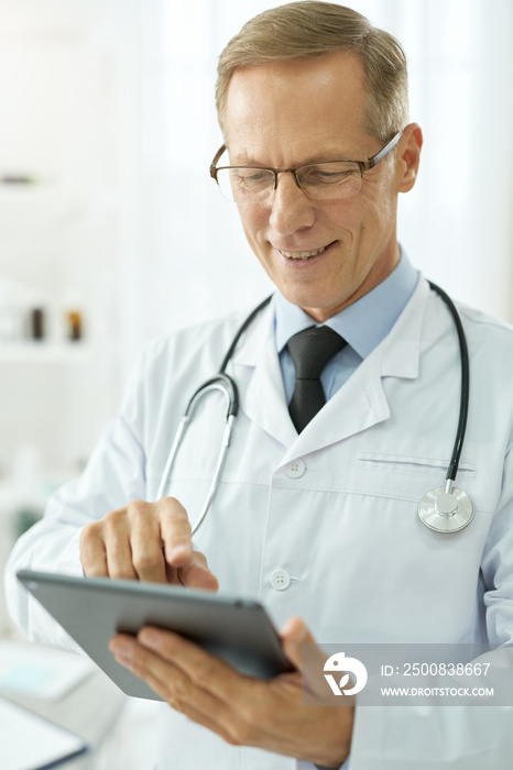 Cheerful male doctor using tablet computer in clinic