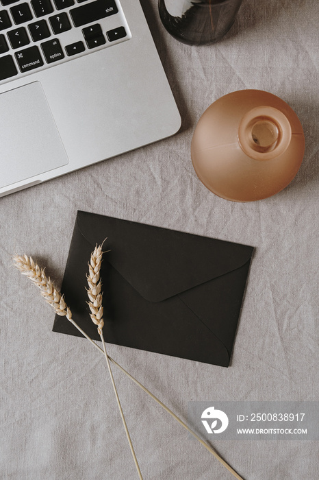 Flatlay of black envelope, laptop, rye / wheat ear stalk and decoration on grey washed linen cloth. Flat lay, top view. Beautiful stylish lifestyle blog, website concept.