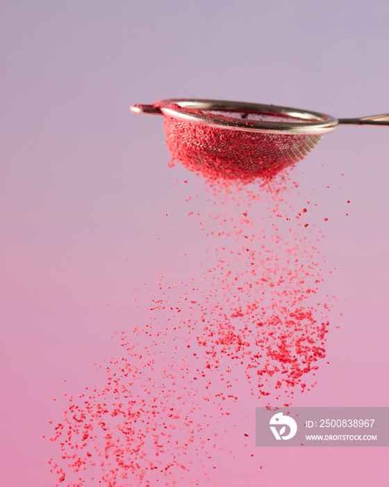 pink berry powder pouring out of a sieve against a pink-purple gradient background