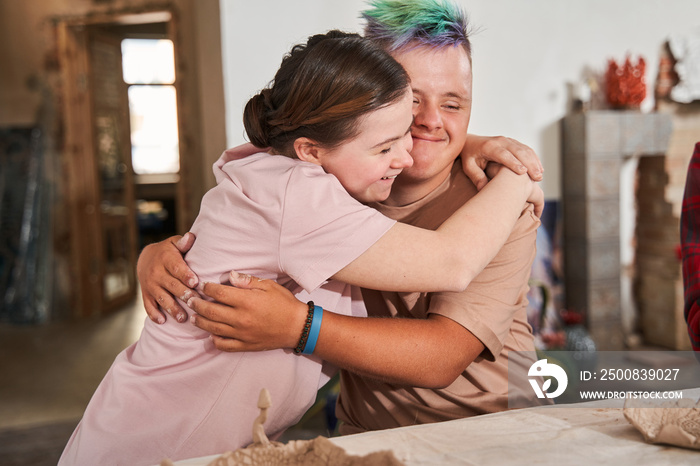 Down syndrome couple embracing and feeling happy during the pottery master class