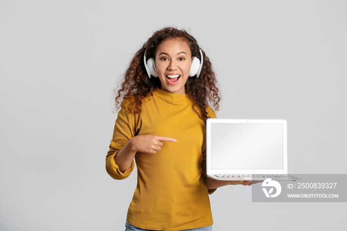 Young woman with laptop and headphones on light background