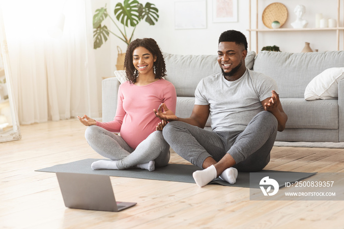 Positive black expecting couple having online yoga class