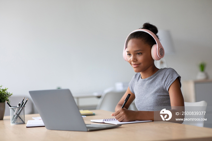 Happy adolescent afro american female student with headphones studying at home watching online lesson