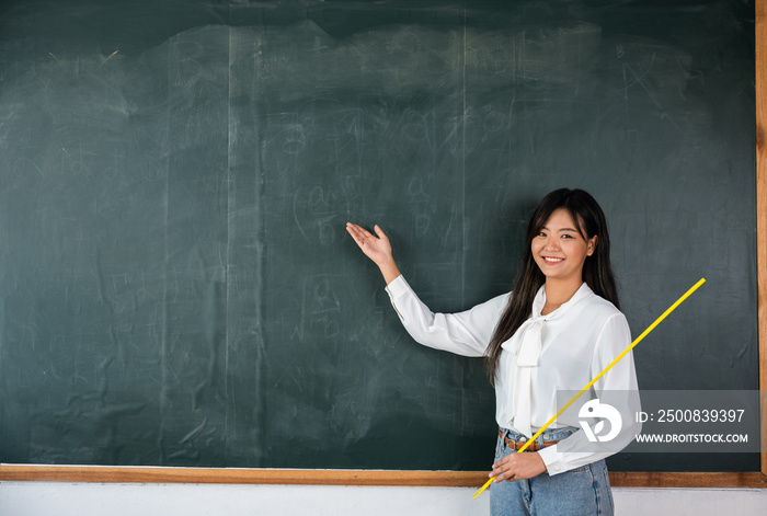 Back to school concept. Happy beautiful young woman standing hold pointer to back board, Asian female teacher smiling with wooden stick pointing to blackboard at school in classroom, Education