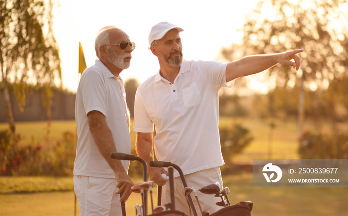 Two older men stand on a golf course and talk.