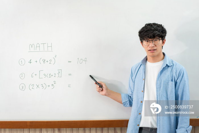 Male tutor standing in front of whiteboard and writing math equations on board to explaining new lesson