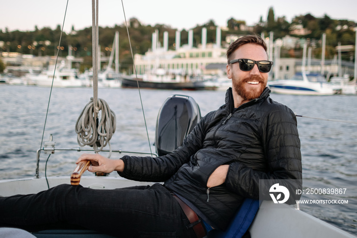 Man in sunglasses drives sailboat at sunset