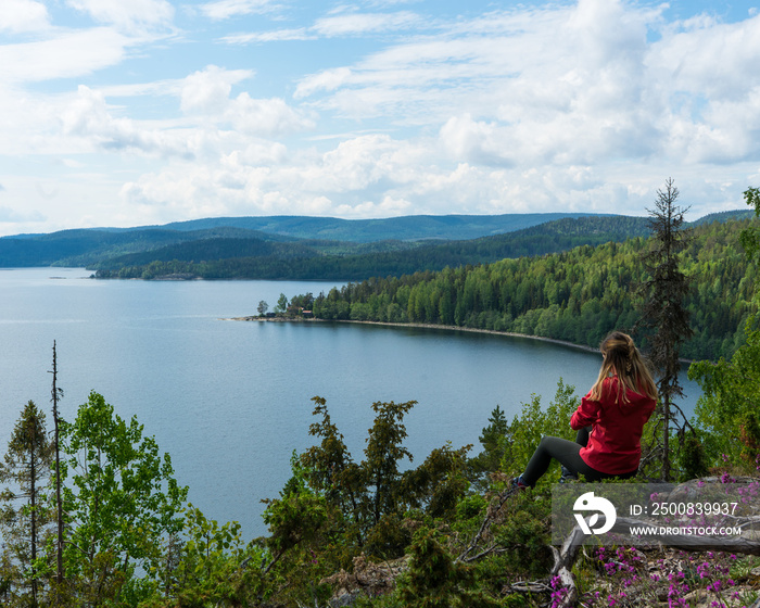 Girl wearing red jacket sitting on top of hill looking out over lakes in the High Coast, Norrland, Sweden