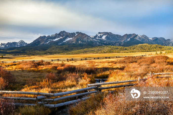 A split rail fence on the border of a large meadow with the Sawtooth mountains in the background, in the fall season near Stanley, Idaho.