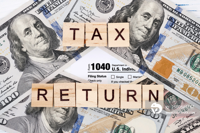 Close-up form 1040, wooden letters tax return and dollar bills. Tax payment and filing concept.