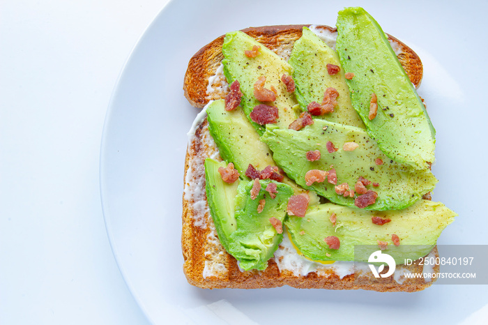 Close up of an avocado toast with bacon bites on a white plate