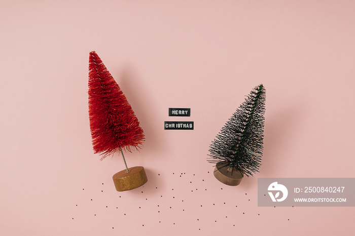 Mini artificial Christmas trees, bottle brush trees for winter decor of green and red color on a pink paper background. DIY New Year ornament. Top viev, flat lay.