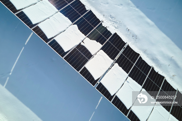 Aerial view of electrical power plant with solar panels covered with snow melting down in winter end for producing clean energy. Concept of low effectivity of renewable electricity in northern region