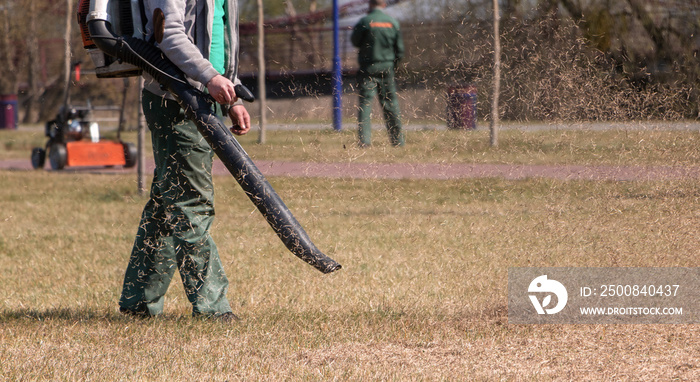 Lawn care. The gardener removes old dried grass from the lawn in the park with a gasoline portable blower.