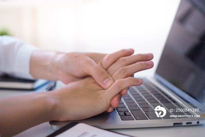 Business woman pressing the middle of her palm with her thumb to relieve pain due to a tendinitis caused by an excessive use of computer.