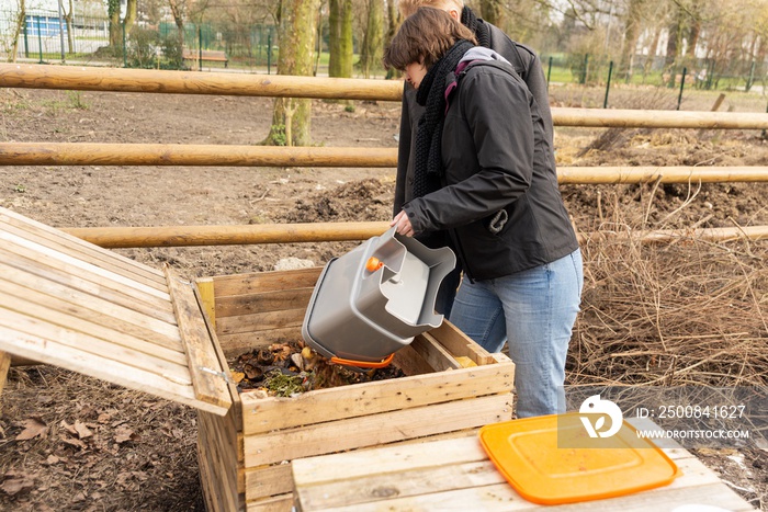 Woman empty organic wastes in wooden compost heap