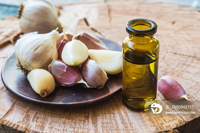 Garlic oil in a glass bottle near ripe garlic on a background of blue old boards. C