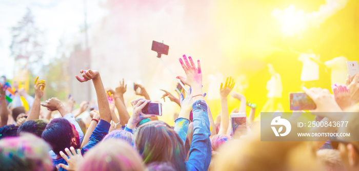 Crowd of people dancing and celebrating Holi festival of colors. People taking photos with mobile phones at color festival