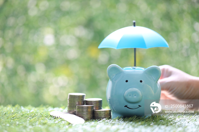 Protection,Piggy bank with hand holding the umbrella and stack of coins money on natural green background, Finance insurance and Safe investment concept