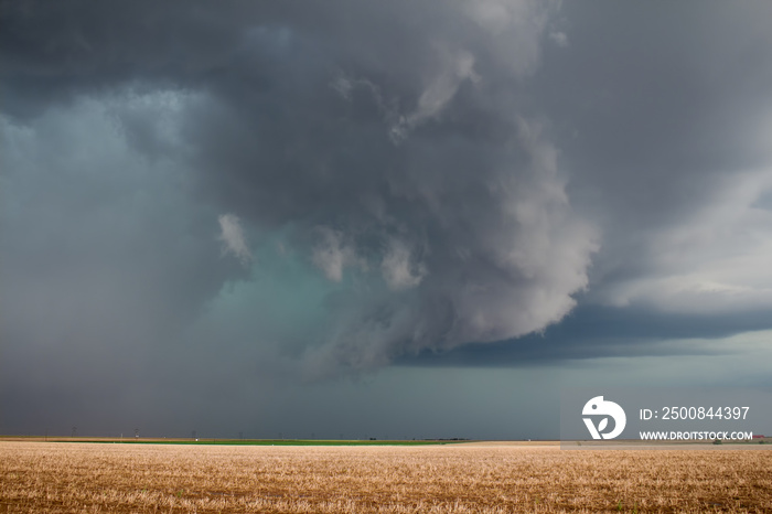 A severe supercell storm containing rain, hail, and damaging winds approaches over farmland.