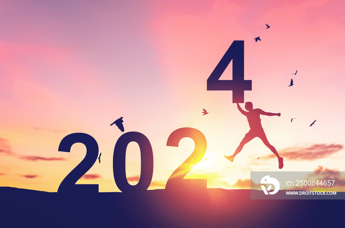 Man jumping on sunset sky with birds flying at top of mountain and number 2024 abstract background. Happy new year and holiday concept.