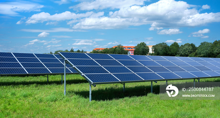 Solar power plant, blue solar panels on grass field under blue sky with clouds