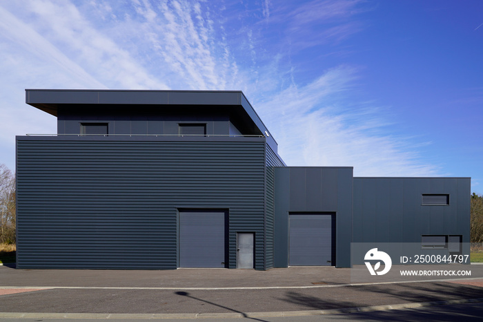 gray large industrial building exterior warehouse grey hangar exterior with rolling gates in blue sky