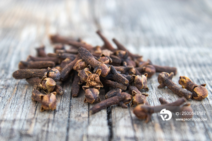 The spice of dried cloves lies on a pile on old wooden boards.