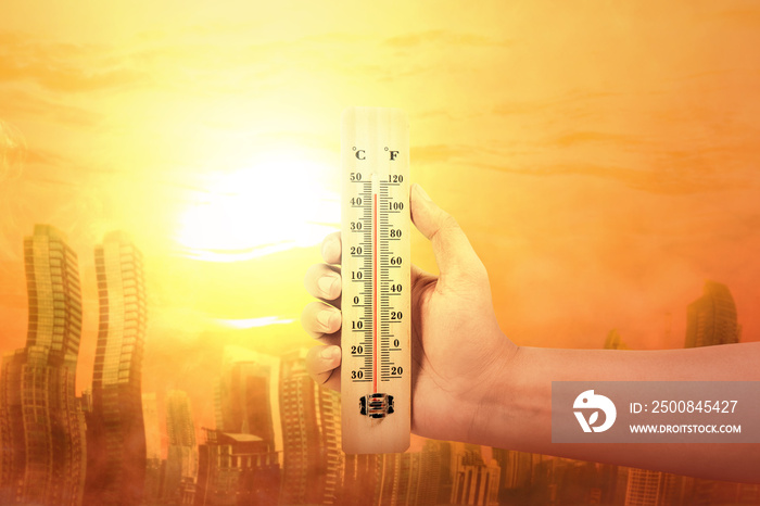 Hand holding thermometer with high temperature on the city with glowing sun background