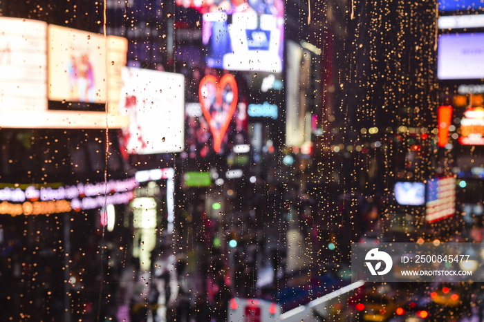 Neon heart seen through rain drops and wet window and background bokeh of traffic and billboards in Times Square, New York City