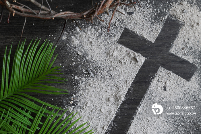 Lent background with cross of ashes, palm leaves and partial crown of thorns on dark wood