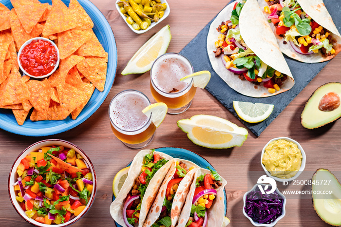 Table with tacos, mango salsa, nachos with sauce, guacamole, lemon beer for Cinco de Mayo celebration party. Appetizers and traditional mexican dishes for family dinner on wooden table top, copy space