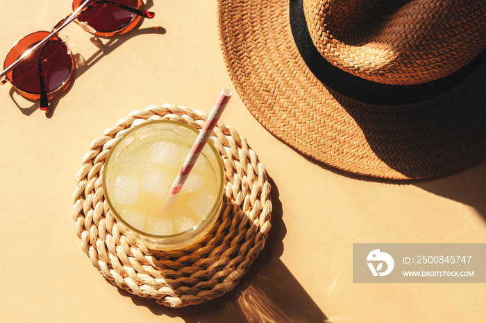 A glass with lemonade and beach accessories on yellow background with harsh shadows, top view