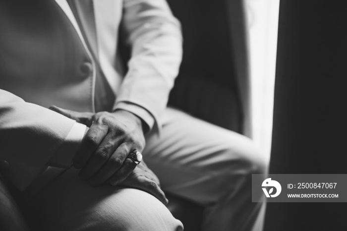 A man in a suit with a signet ring on his little finger sits by the window, close-up, black and white