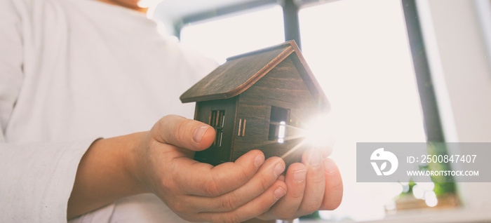 Kid holding wooden toy house in hands. Adoption concept. Desire to have your own home and family.