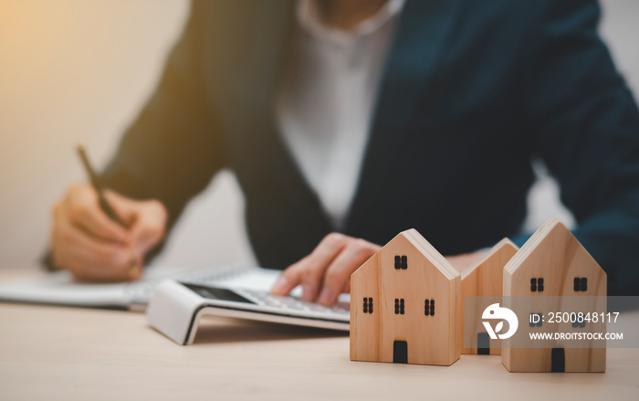 Businessman hand write note on paper with mini wood house model from model on wood table, Planning buy Real Estate, Planning to buy property. concept of Choose the best.