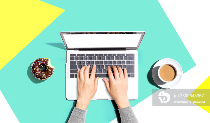 Person using a laptop computer with a donut and a cup of coffee - Flat lay