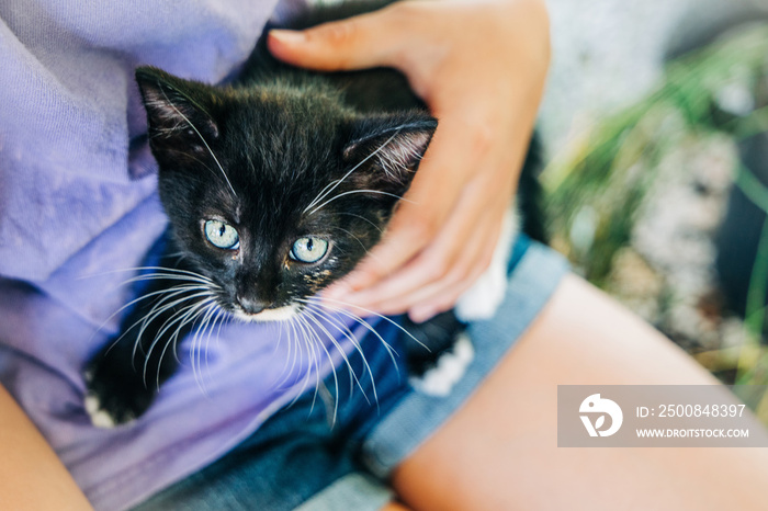 Child holding Small black kitten with blue eyes