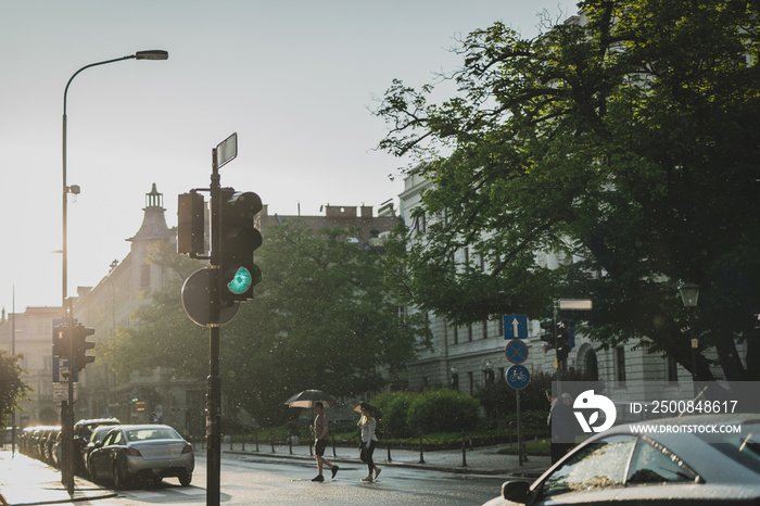 Dangerous jaywalking on a city street while cars have green light. Dangerous situation crossing the road in the city illegally in bad conditions - rain, light from behind, slippery road etc.