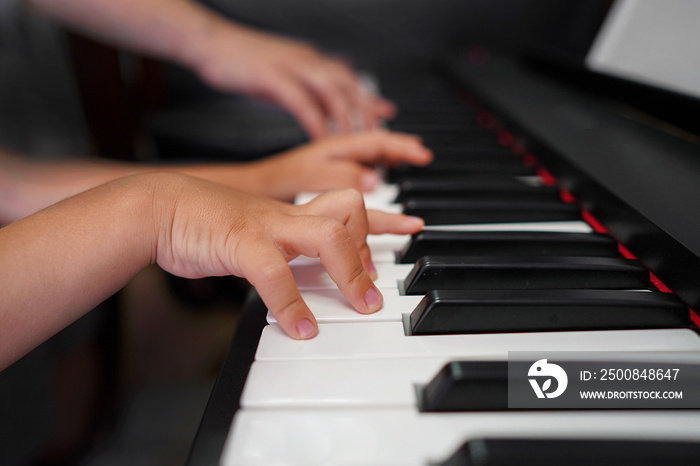 Children’s hands and teacher’s hands on the piano keys. ?hildren’s hands plays the piano, learning a lesson, black and white keys. Training on a synthesizer. Selective focus