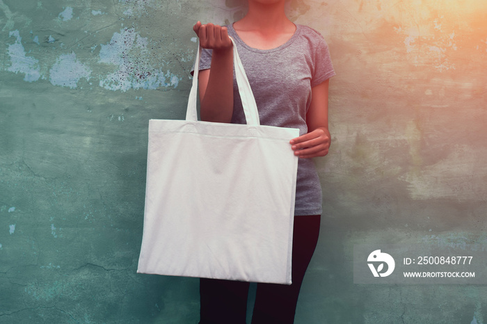 young woman holding cotton bag on wall background. eco concept