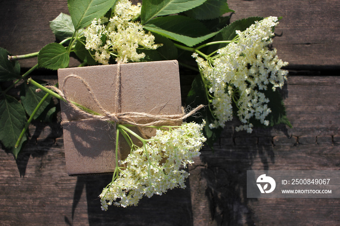 Brown craft gift box decorated with natural herbs and flowers on old wooden background with copy space. Floral decor elements. Father`s day gift concept.