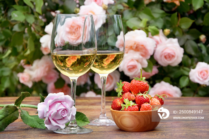 Two glasses of wine with strawberries and a rose on a background of roses.