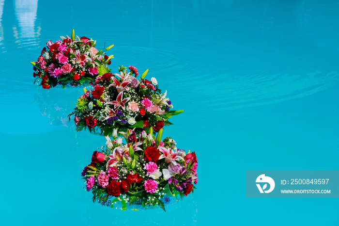 Fresh garden roses on the blue water of a swimming pool on a warm summer day.